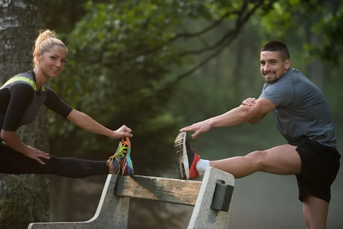 Młoda para rozciąga się przed bieganiem w zalesionym terenie leśnym
