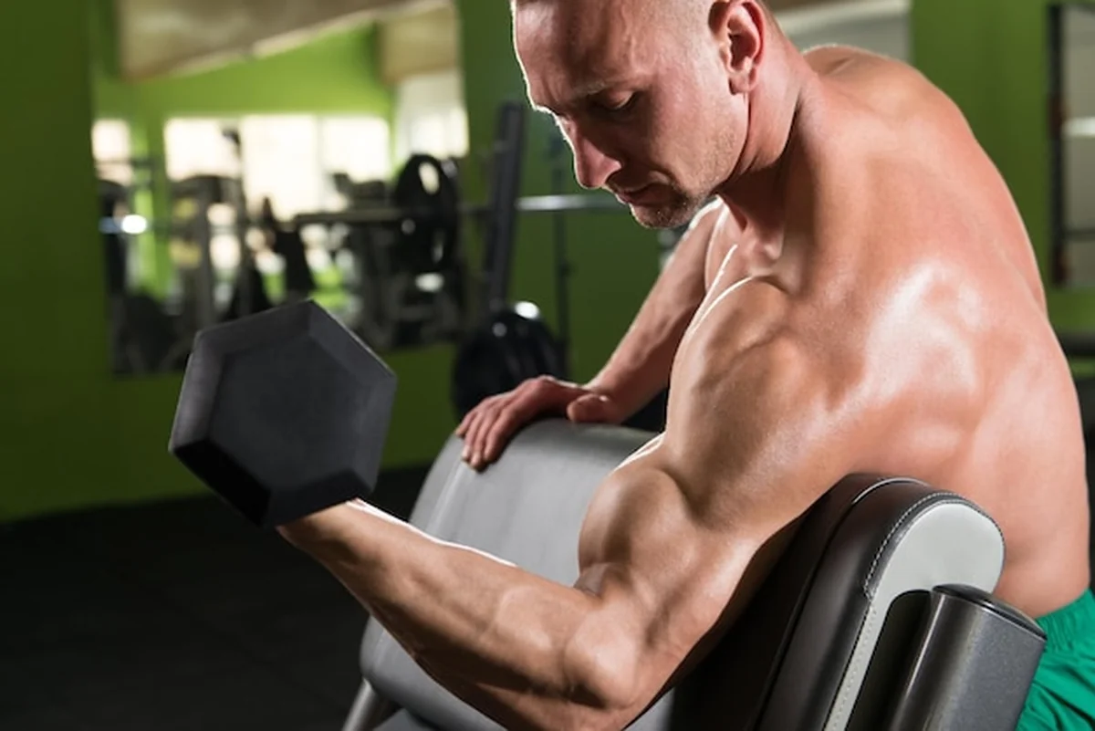 Młody mężczyzna ćwiczący bicepsy z hantlami na siłowni