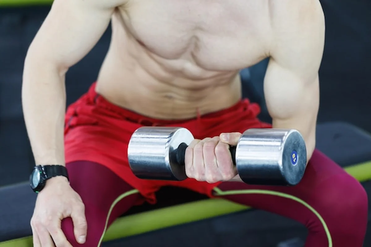 Mężczyzna topless podnoszący hantle na siłowni