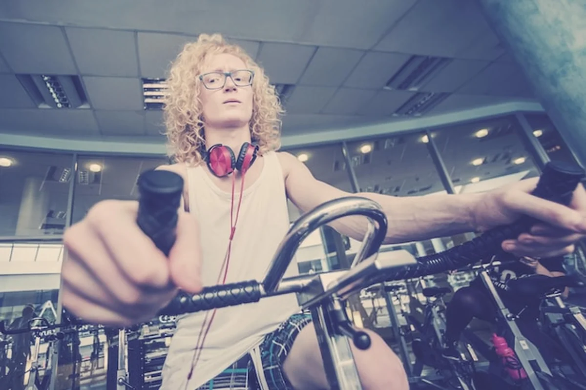 Blondyn trenuje na rowerze stacjonarnym z czerwonymi słuchawkami