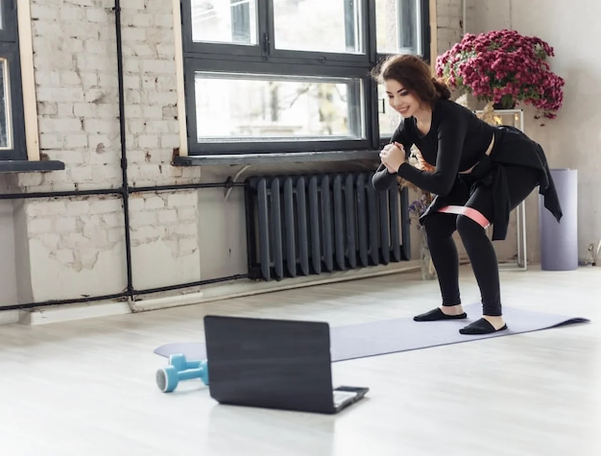 Uśmiechnięta kobieta w stroju sportowym oglądająca filmy fitness na laptopie