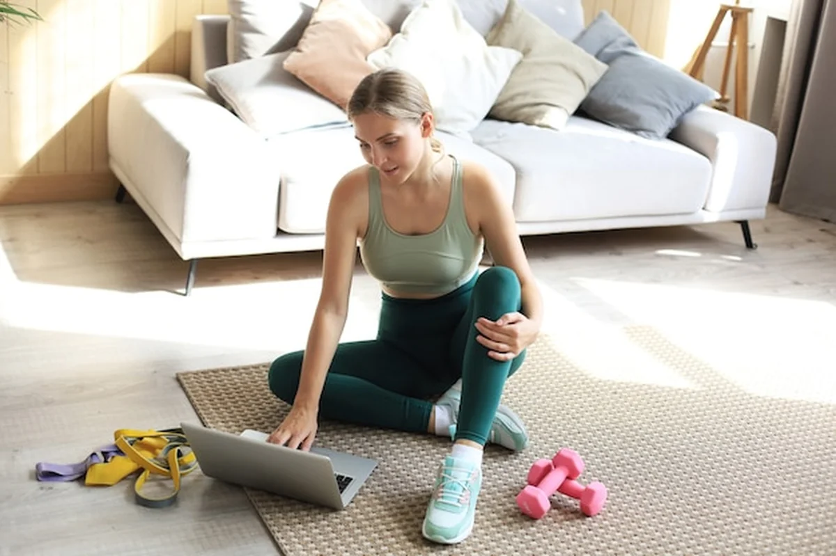 Sportowa kobieta z hantlami i laptopem na podłodze w salonie
